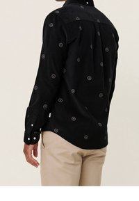 Maglietta nera a maniche lunghe con una texture liscia, caratterizzata da motivi ricamati circolari in colori variati. Polsini con bottoni e orlo curvo.