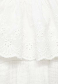 White cotton fabric with broderie anglaise detailing at the hem. The texture is soft with delicate, scalloped edges and subtle patterns.
