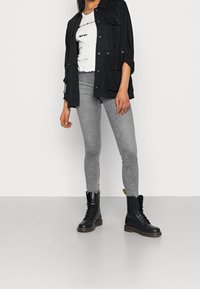 Sort letvægtsjakke med lommer, hvid tie-dye skjorte, grå skinny jeans og sorte snørebånds kampstøvler.