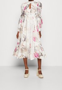 Robe midi florale avec des manches bouffantes, décolleté en forme de trou de serrure et bord blanc. Présente des motifs aquarelle roses et beiges sur un fond clair.