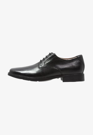 Black leather dress shoe with a rounded toe, smooth texture, six eyelets for laces, and a low profile rubber sole.