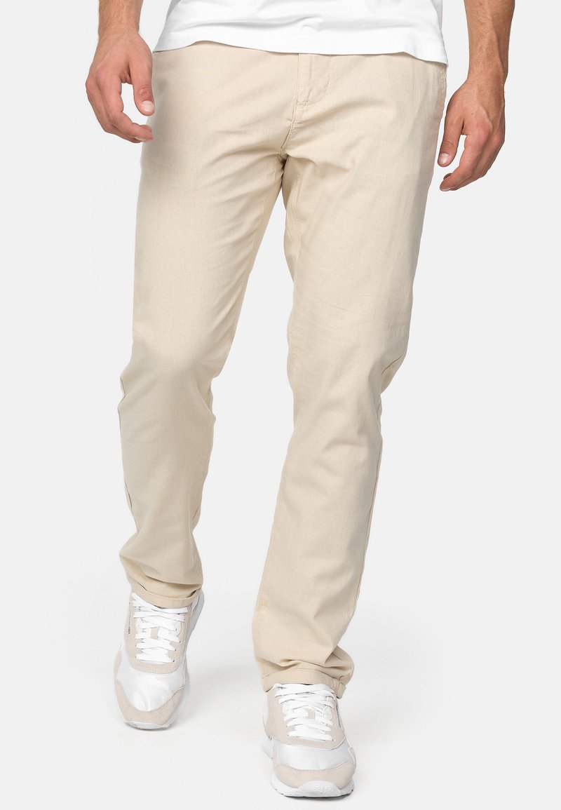 Pantalons beige à jambe droite en tissu léger, présentant une texture douce et des détails de couture minimaux, associés à des baskets blanches.