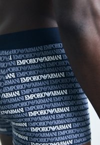 Emporio Armani bokseritrid, millel on tumesinine alus ja valged brändilogod, mis korduvad. Pehme kangas, mis pakub mugavat istuvust ja elastne vöökoht.
