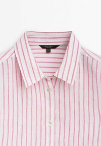 Chemise blanche à col avec des rayures verticales roses et deux boutons blancs visibles à l'avant.