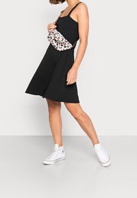 Svart ärmlös klänning i A-linjeform, kombinerad med vita högskftsneakers och en liten korsväska med leopardtryck.