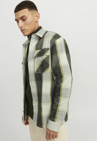 Camicia a maniche lunghe a quadri in tonalità di nero, bianco e verde. Presenta taschini sul petto, chiusura con bottoni e una vestibilità rilassata. Texture morbida.
