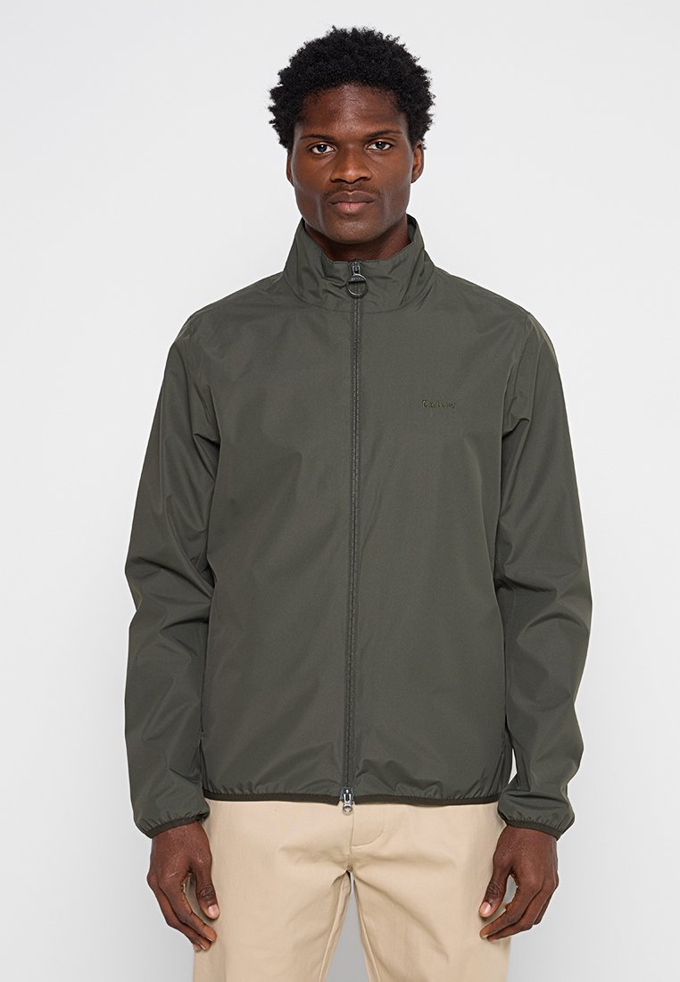 Giacca leggera di colore verde scuro con colletto alto, zip frontale completa, polsini elasticizzati e un logo sul petto. Tessuto liscio e resistente all'acqua.