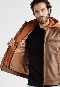 Bruine leren jack met capuchon, voorzien van een oranje binnenvoering, voorzakken en een ritssluiting. Gladde textuur en op maat gemaakte ontwerpen.