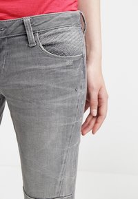 Vaqueros de mezclilla gris con un diseño ajustado, que presentan un área de bolsillo texturizada, costuras sutiles y un acabado liso.