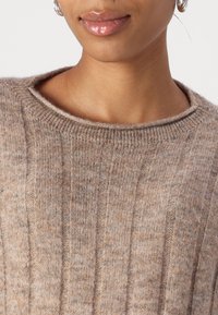 Beige kötött pulóver bordázott textúrával, széles kerek nyakkal és puha, kényelmes anyagból készült. A minta diszkrét és egységes.