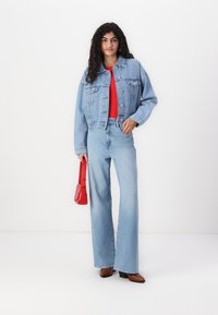 Jeansjacka med kort design, långa ärmar, parat med högmidjade, vida ljusblå jeans; röd topp och liten röd handväska.