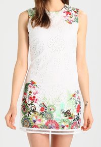 Vestido blanco sin mangas con estampados florales, detalles troquelados, una silueta ajustada y un dobladillo con flecos.