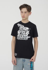 T-shirt in cotone nero con grafica bianca con la scritta "BORN TO SKATE" e ulteriori disegni a tema skate. Girocollo, maniche corte, vestibilità rilassata.