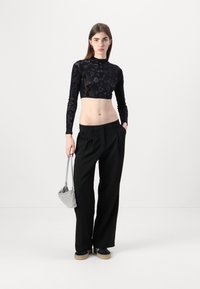 Svart blomstret blondelongsleeve crop top kombinert med høytlivede svarte plisserte bukser. Modellen holder en sølvfarget mini-håndveske. Plattform sko er inkludert.