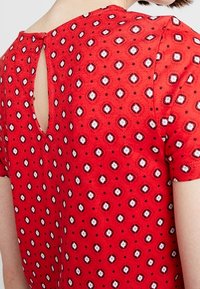 Top corto rosso a maniche corte con retro a occhiello. Presenta un motivo di piccoli diamanti bianchi e neri con una texture di tessuto liscia.
