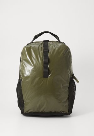 Sac à dos olive avec une surface brillante, doté d'une sangle centrale et de poches latérales en mesh. Détail de fermeture éclair sur le côté. Tissu texturé.