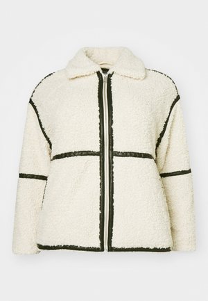 Bijela polar jakna s teksturiranim površinom, s crnim obrubom duž šavova, zatvaranjem na patentni zatvarač i ovratnikom.