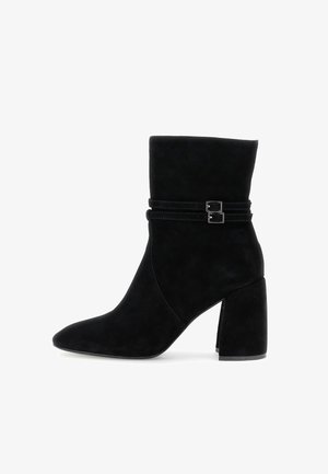 Botas de ante negras hasta el tobillo con punta afilada, caña baja y desenfadada, y dos correas decorativas con hebillas en el tobillo. Tacón cuadrado.