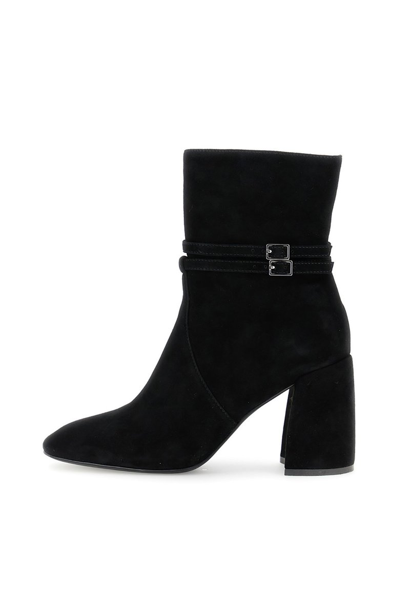 Botas de ante negras hasta el tobillo con punta afilada, caña baja y desenfadada, y dos correas decorativas con hebillas en el tobillo. Tacón cuadrado.