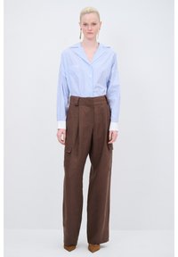 Blau-weißer gestreifter Button-Up-Hemd mit langen Ärmeln, kombiniert mit braunen weit geschnittenen Cargo-Hosen mit Seitentaschen und einer strukturierten Oberfläche.