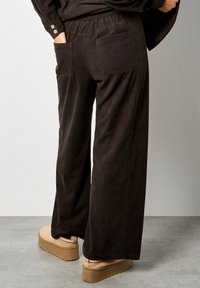 Wijduitlopende, donkerbruine corduroy broeken met een elastische tailleband, achterzakken en een zacht textuur. Stevige platform schoenen maken de look compleet.