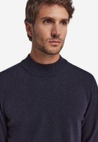 Marinblå stickad tröja med hög halsringning. Mjuk textur, figursydd design och subtil ribbstickning vid kragen och ärmslut.