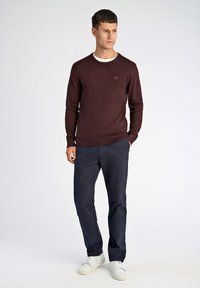 Burgundowy sweter z długimi rękawami i ściągaczami, założony na biały t-shirt z okrągłym dekoltem, w połączeniu z granatowymi spodniami i białymi butami.