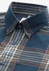 Camisa de cuadros en tonos azules, verdes y marrones. Presenta un cuello estructurado y una tela interior contrastante con un patrón de puntos.