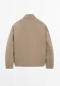 Beige jakke lavet af glat stof med klassisk krave, lange ærmer og en lige kant med subtile syningsdetaljer.