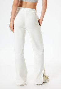 Witte uitlopende joggingbroek met een trekkoord in de taille, zijslits aan de zoom en een zachte stofstructuur. Minimalistisch ontwerp zonder zichtbare patronen.