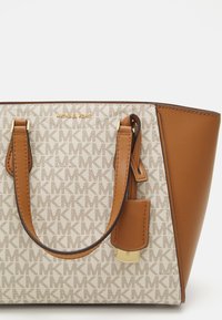Borsa tote beige e crema con un motivo testurizzato, dettagli dorati, manici doppi e un logo. Presenta una forma strutturata e blocchi di colore distintivi.