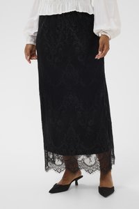 Fekete csipke maxiszoknya virágmintákkal, hullámos szegéllyel és bonyolult részletezéssel. Fekete magassarkú papuccsal és fehér blúzzal viselve.