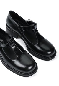 Czarne skórzane buty z zapięciem typu T, zaokrąglonym noskiem, niskim blokowym obcasem i widocznym przeszyciem. Gładka powierzchnia z wypolerowanym wykończeniem.