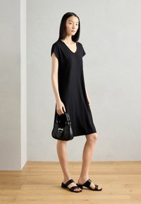 Black V-neck dress with short sleeves, smooth texture, paired with black block-heel sandals and small handbag with silver accents.