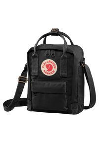 Svart ryggsäck gjord av slitstarkt tyg, med dubbla handtag på toppen, en justerbar rem, framficka och en cirkulär logotyp-patch.