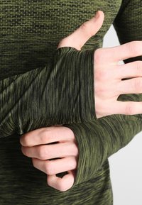 Grön långärmad topp i strukturerad tyg med ett subtilt randigt mönster. Har tumhål vid ärmsluten och en figurnära design.