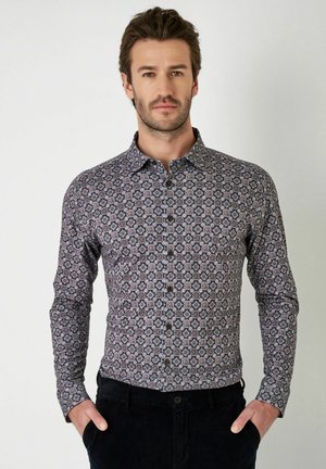 Langarmhemd mit dunkelblauem Hintergrund, das ein geometrisches Muster in Weiß und Kastanienbraun aufweist, mit einem Button-down-Kragen und sichtbaren Knöpfen.