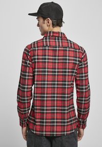 Rød og svart rutete flanellskjorte med lange ermer, knappelukking ved håndleddene og krage. Brukt med en svart caps som viser et mønstrete tekstur.