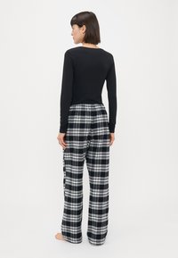 Sort langærmet top parret med rutede pyjamasbukser, der har et hvidt og gråt ternet mønster, elastisk talje og løs pasform.