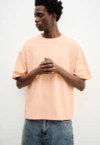 Ferskenfarvet bomulds t-shirt med korte ærmer, rund hals, og afslappet pasform, parret med højtaljede blå denim jeans.