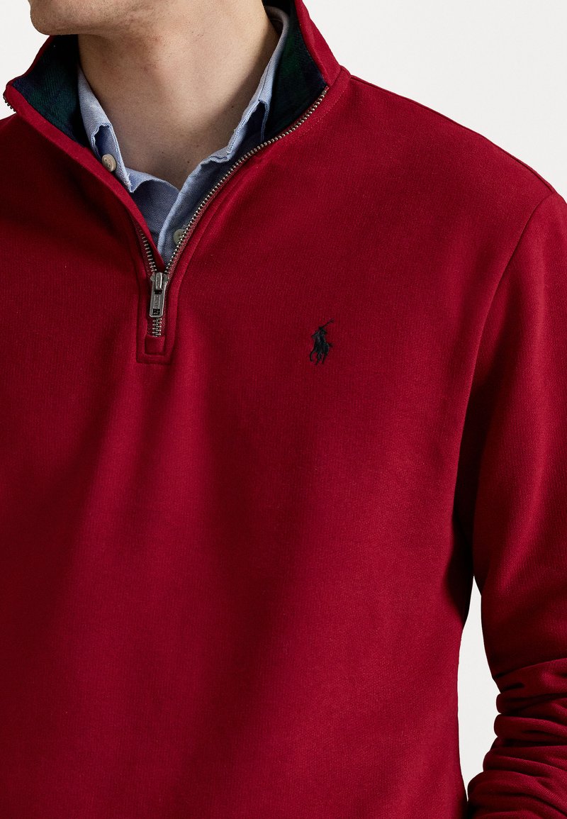 Pullover rosso con zip in misto cotone, con colletto verde a contrasto. Caratterizzato da un logo ricamato sul petto. Texture liscia.