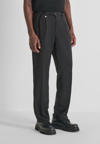 Pantalones negros con un diseño de pierna recta, textura suave, bolsillos laterales y lazos para el cinturón. Combinados con zapatos negros tipo cordón.