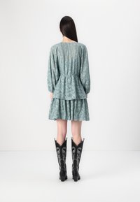 Lace-overlay kjole i teal med peplum liv og lagdelt skjørt. Kombinert med svarte cowboy støvler med sølvdetaljer.