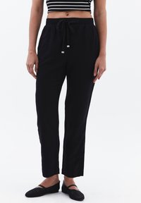 Schwarze, leichte, gerade geschnittene Hose mit Gummizugbund und Seitentaschen, aus strukturiertem Stoff ohne sichtbare Muster.