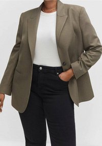 Blazer à carreaux vert olive avec un design structuré, fermeture par un bouton unique et deux poches avant, associé à un haut blanc et un jean noir.