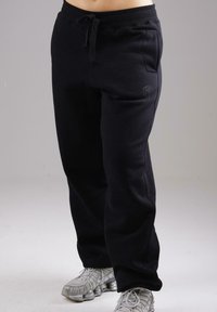 Person wearing black sweatpants with front pockets and gray athletic shoes, standing against a neutral background.