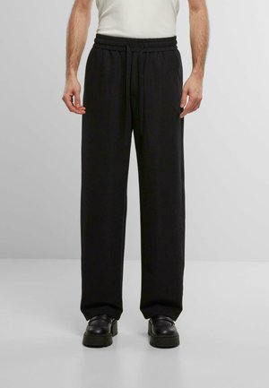 Black, loose-fitting trousers made of soft fabric with an elastic waistband and drawstring. Flat pockets on sides and subtle texture.