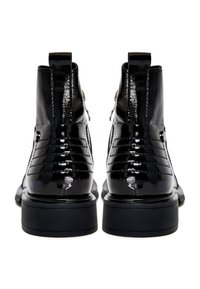 Botas de tobillo de charol negro con acentos acolchados, textura suave, forma curvada y suelas de goma sólidas. Detalle de diseño con cierre de cremallera lateral.