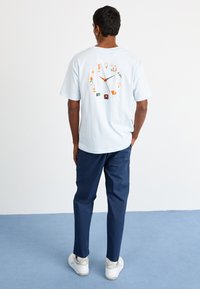 Lyseblå bomulds t-shirt med et farverigt urskivegrafik på ryggen, parret med marineblå bukser og hvide sneakers.