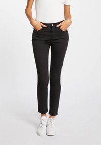 Zwarte skinny jeans met een middelhoge taille, voorzien van een voorste knop en ritssluiting, zijzakken en een gladde stoftextuur. Gecombineerd met witte sneakers.